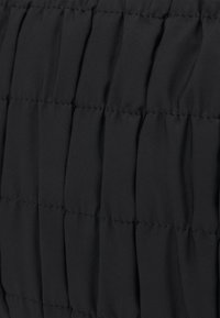 Tissu matelassé noir avec des coutures verticales, créant un motif texturé avec une apparence douce et légère. Idéal pour les vêtements d'extérieur.