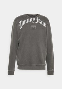 Šedá mikina s dlouhými rukávy, kulatým výstřihem, bílým logem "Tommy Jeans" přes hrudník a žebrovanými manžetami a spodním lemem. Měkká textilie.