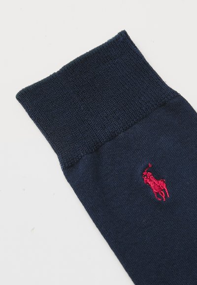 Calcetín azul marino con un puño acanalado y un logo rojo bordado. El material parece suave y tejido, con un diseño sin costuras.