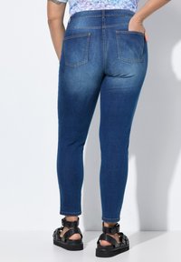 Modré džíny skinny s vysokým pasem, s dvěma zadními kapsami a hladkou texturou. Odpovídají černým sandálům na podpatku.