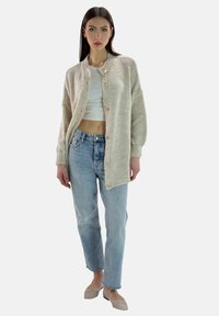 Beige stickad kortärmad kofta med rund halsringning och knappstängning, i kombination med ljusblå raka jeans och beige balettklackar.