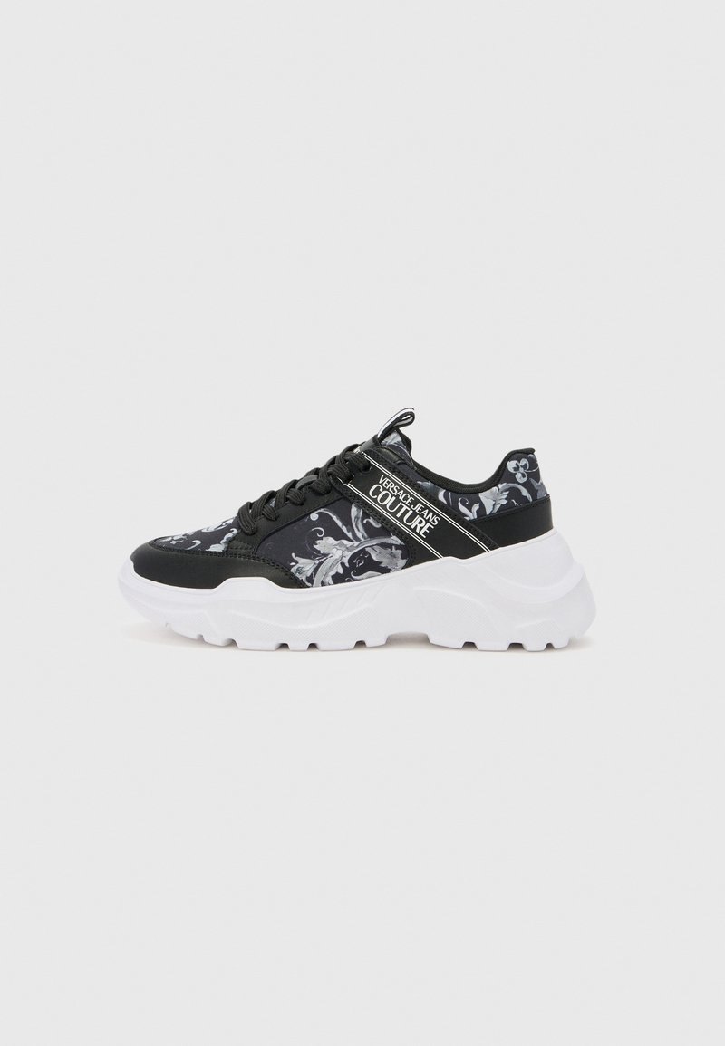 Scarpe sportive nere con motivo floreale e suola bianca spessa. Presentano lacci neri e una fascia con il logo sul lato. Parte superiore in tessuto texture.