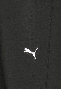 Černé sportovní legíny vyrobené z elastického materiálu s bílým logem Puma, švem a hladkým povrchem.