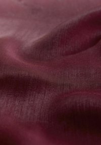 Bordó szövet sima, enyhén fényes textúrával. Finom színárnyalat-változásokkal és hullámos redőkkel rendelkezik, amelyek a drapírozhatóságot jelzik.