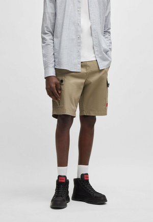 Khaki cargo shorts with side pockets, a slim fit, textured fabric. Paired with a striped long-sleeve shirt and black high-top sneakers.