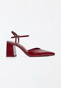 Chaussure femme en cuir rouge à bout pointu, talon bloc et bride à la cheville avec boucle sur fond blanc.
