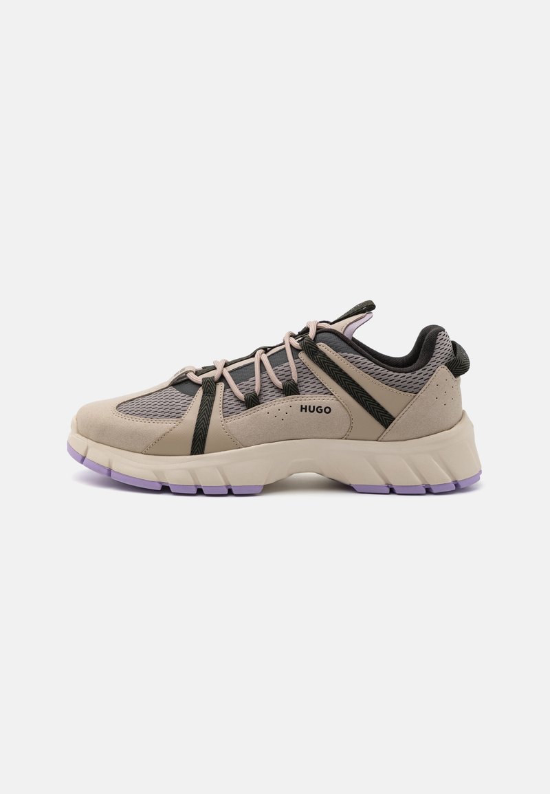 Beige and black athletic shoes featuring a mesh upper, rubber sole, purple accents, and black lacing system. Logo displayed on the side.