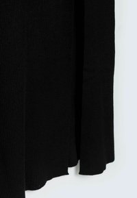 Tissu tricoté noir avec une texture côtelée, présentant un ourlet asymétrique et une finition lisse. Sans quincaillerie visible ni motifs.