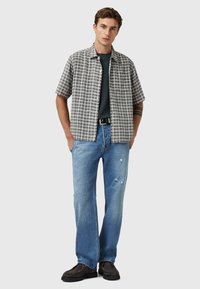 Kurzärmliges kariertes Hemd in Grau und Weiß, kombiniert mit einem dunkelgrauen T-Shirt, hellblauen distressed Jeans und dunklen Schuhen. Einfaches, lässiges Design.