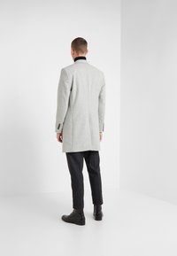 Abrigo de lana gris con cuello negro, diseño entallado y mangas largas, combinado con pantalones oscuros y botas negras.