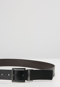 Fibbia in metallo argentato rettangolare con una cintura nera in pelle con finitura testurizzata e fodera in ecopelle grigia scura.