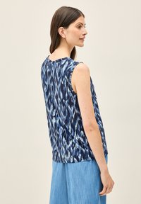 Ärmelloses Shirt in Marineblau mit hellblauem abstraktem Muster, Rundhalsausschnitt, drapiertem Material und lockerer Passform, kombiniert mit hellblauen Hosen.