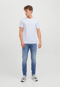 T-shirt blanc à manches courtes associé à un jean bleu clair et des baskets blanches sportives. Design simple, texture lisse, coupe classique.