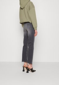 Jeans de mezclilla gris con corte recto, combinados con una sudadera verde. Mules negros con detalles de borlas completan el conjunto.