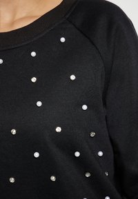Maglione nero realizzato in un tessuto testurizzato con applicazioni di strass e perle disposte in un motivo sparso sulla parte anteriore.
