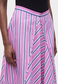 Femme portant une jupe taille haute avec des rayures verticales et diagonales roses, blanches et bleues, associée à un haut noir.