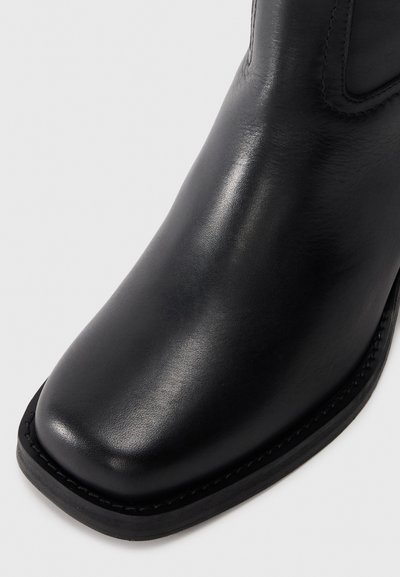 Black leather ankle boot with a smooth texture, square toe, and stitched accents along the sole for added durability.