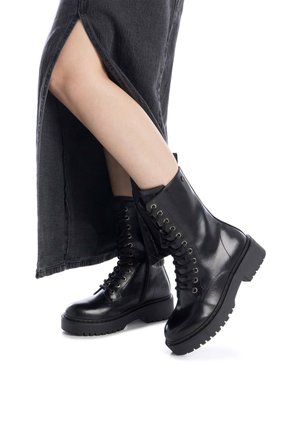 Botas de combate negras de cuero con suela gruesa, punta redonda y cordones en la parte frontal; textura suave con ojales metálicos y un cuello acolchado.