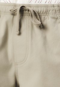 Beige shorts with an elastic waistband and drawstring. Soft fabric, side pockets, and stitched detailing along the seams.