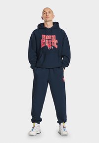 Granatowy komplet z kapturkiem i dresami, wykonany z miękkiego materiału, z dużą czerwoną grafiką "ATHLETIC" na przodzie i dopasowanym wzorem dresów.