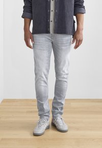 Ljusgrå jeans med slim fit och subtil blekning, kombinerade med grå sneakers. Skjortan är marinblå kordflana med ett rutigt mönster under.