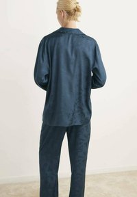 Mörkblå satin tvådelat set med en långärmad skjorta med knäppning och krage samt matchande byxor med subtilt blommönster.