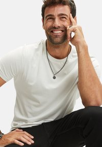 Witte korte mouwen t-shirt met een gladde textuur, gecombineerd met zwarte broek. Een ketting met een cirkelvormige hanger wordt gedragen.