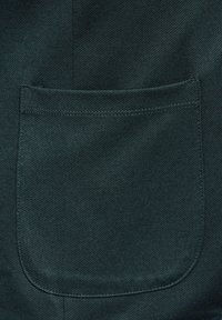 Tejido verde oscuro con una textura que recuerda al denim. Presenta un bolsillo rectangular con esquinas redondeadas y costuras visibles a lo largo de los bordes.