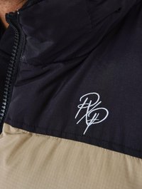 Giacca da uomo con un design a blocchi di colore, con la parte superiore nera e quella inferiore color sabbia. Include tessuto testurizzato e logo ricamato.