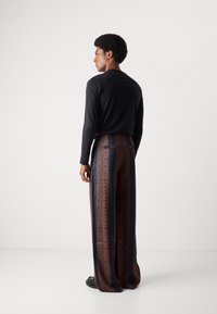 Camisa de manga larga negra y pantalones anchos de estampado en azul marino oscuro con diseños geométricos naranjas. Textura suave y corte relajado.