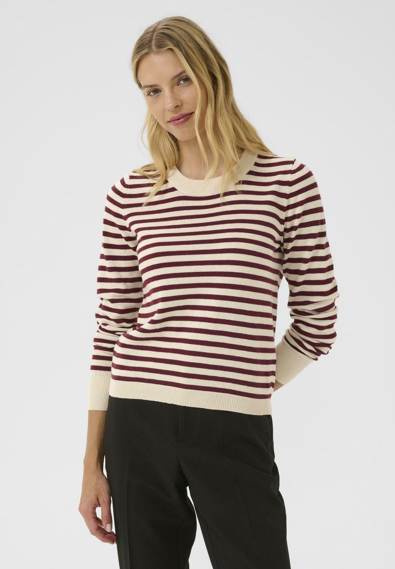 Pull crème avec des rayures horizontales bordeaux, col rond à côtes et manches côtelées. Tissu doux. Associé à un pantalon noir.