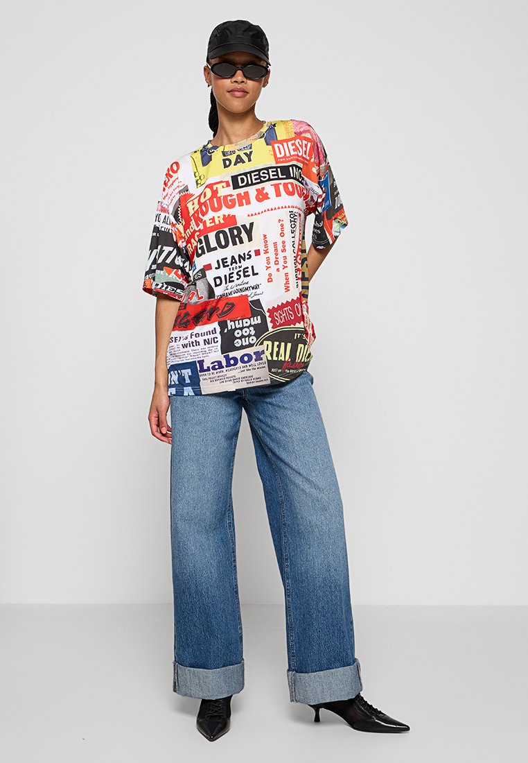 Übergrößent-Shirt mit einem mehrfarbigen Grafikdruck auf weißem Hintergrund, kombiniert mit weit geschnittenen blauen Jeans und schwarzen spitzen Stiefeln.