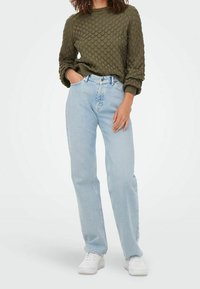 Maglione verde oliva con texture e design trapuntato, abbinato a jeans a gamba dritta azzurri e sneakers bianche.