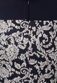 Il tessuto a righe blu navy e crema presenta motivi floreali e dettagli intricati. La parte superiore è di un blu navy uniforme con una cucitura centrale e una cerniera.