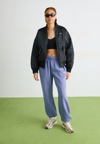 Crna bomber jakna, crni crop top, svijetloplave trenirke i tenisice sa zlatnim naglascima. Dodaci uključuju tamne sunčane naočale.