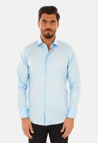 Camicia azzurra a maniche lunghe con chiusura a bottoni, colletto a punta e polsini azzurri a contrasto. Tessuto liscio con una sottile texture.