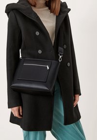 Schwarze Umhängetasche aus glattem Leder mit vordertaschenreißverschluss, rechteckiger Form und verstellbarem Riemen.