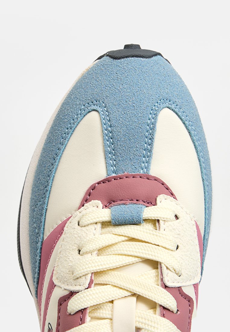 Zapatilla con una punta de ante azul, cuerpo de piel crema, acentos rosas y cordones crema. Cuenta con un collar acolchado y material texturizado.