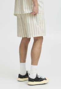 Stripete beige shorts laget av bomull, med vekslende tynne mørke linjer. Kombinert med svarte sneakers og hvite ankelsokker.