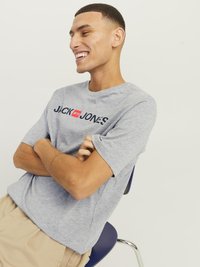 Grå bomull t-skjorte med korte ermer og rund hals, prydet med "JACK & JONES" logo i svart og rødt over brystet.