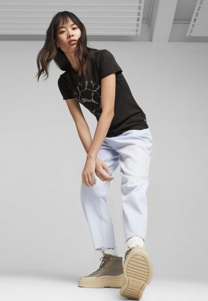 T-shirt nera con stampa grafica, jeans a gamba larga blu chiaro e sneaker alte color beige con suola texturizzata e design con lacci.