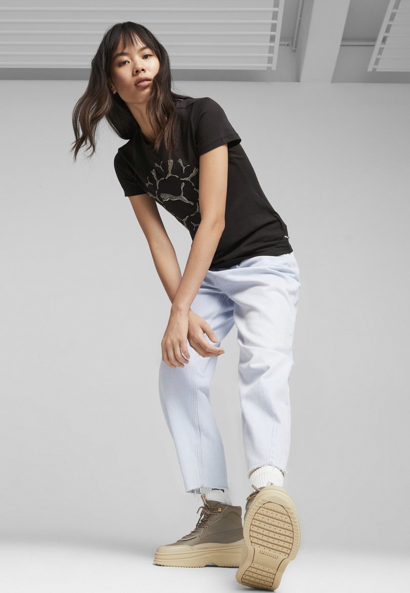 Camiseta negra con estampado gráfico, jeans de pierna ancha en azul claro y zapatillas altas en color tostado con suela texturizada y diseño con cordones.