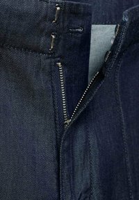 Jean en denim bleu avec fermeture éclair, présentant une texture lisse, un lavage foncé et des accents en métal à la taille et à la fermeture éclair.