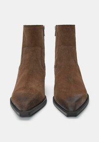 Kastanjasägs ankle boots med spetsig tå, siddragkedjor och svart gummisula. Slät textur med subtila variationer i färg.