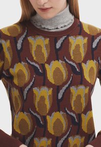 Maglione lavorato a maglia con motivo floreale di tulipani gialli su sfondo borgogna. Include un colletto alto grigio a volant sotto.