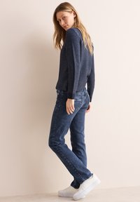Maglione a maniche lunghe con motivo navy abbinato a jeans blu scuri e sneaker bianche. Il tessuto sembra morbido e la vestibilità è rilassata con dettagli di cucitura visibili.