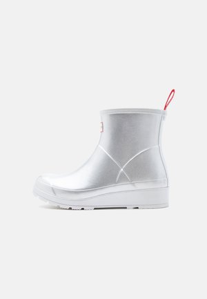 Strieborná gumová pršiplášťová topánka do výšky členku s bielou podrážkou a červeným textilným pútkom vzadu.
