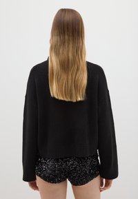 Schwarzer, übergroßer Strickpullover mit strukturierter Oberfläche; kombiniert mit figurbetonten, glänzenden schwarzen Pailletten-Shorts, die eine elegante Silhouette betonen.