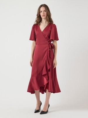 Red satin wrap dress with short puff sleeves. Asymmetrical ruffle hem and tie at the waist. Paired with black pointed heels.
