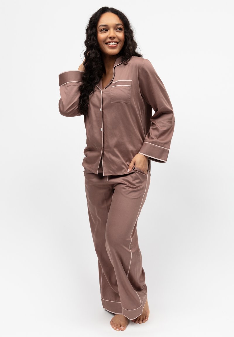 Set di pigiama marrone in tessuto morbido, con top con bottoni e taschino sul petto bordato di bianco, e pantaloni ampi.